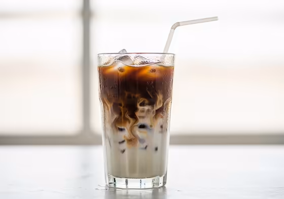 A tall, refreshing glass of iced vanilla latte with condensation on the outside, showing layers of coffee and milk swirling together.