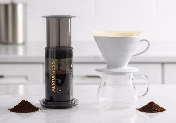 An AeroPress coffee maker and a Hario V60 pour-over dripper sitting side-by-side on a countertop, ready for brewing.