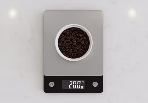 A digital kitchen scale with a small bowl of whole coffee beans on it, displaying the weight.