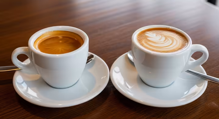 A single and a double espresso shot side-by-side on a wooden table, showing the difference in volume.