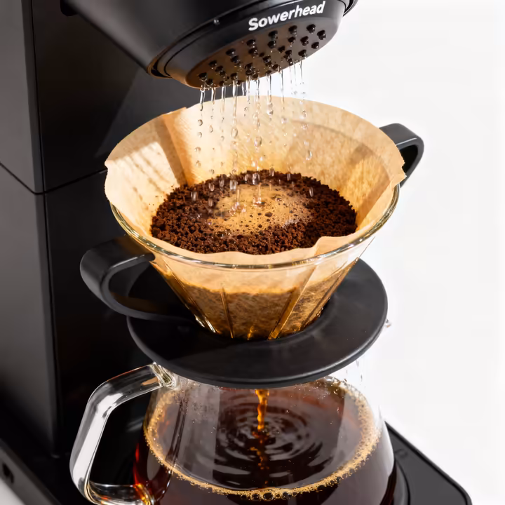 A modern drip coffee machine brewing coffee, with hot water dripping over the coffee grounds in the filter into a glass carafe below.