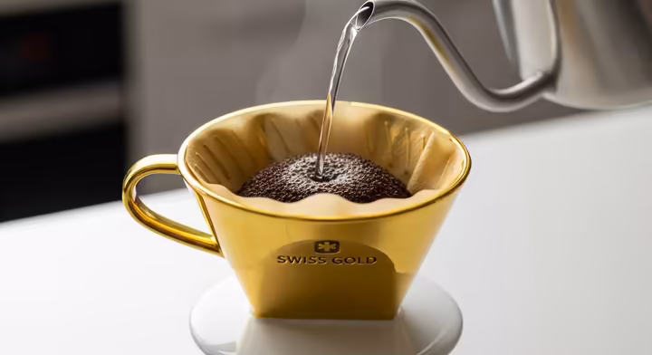 A Swiss Gold cone filter inside a ceramic pour-over dripper with coffee being poured into it.